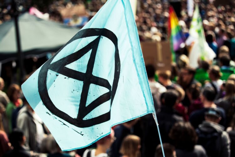 Een vlag van Extinction Rebellion wappert boven een menigte demonstranten